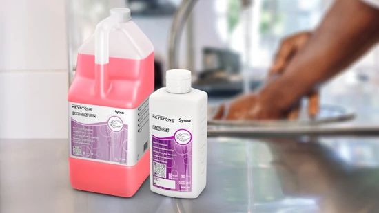 Keystone Hand Soap and Keystone Des (hand disinfectant) sat on side of kitchen surface with someone washing their hands in the background
