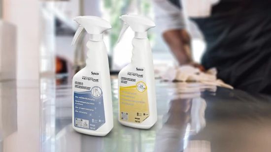 Keystone Multi Surface Spray and Glass Spray sat on kitchen work surfaces with someone wiping a surface in the background